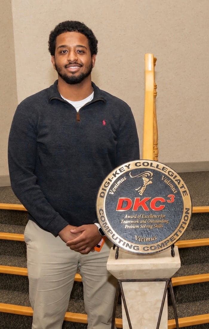 Markose Mesay standing beside the Digi-Key Collegiate Computing Competition award plaque.